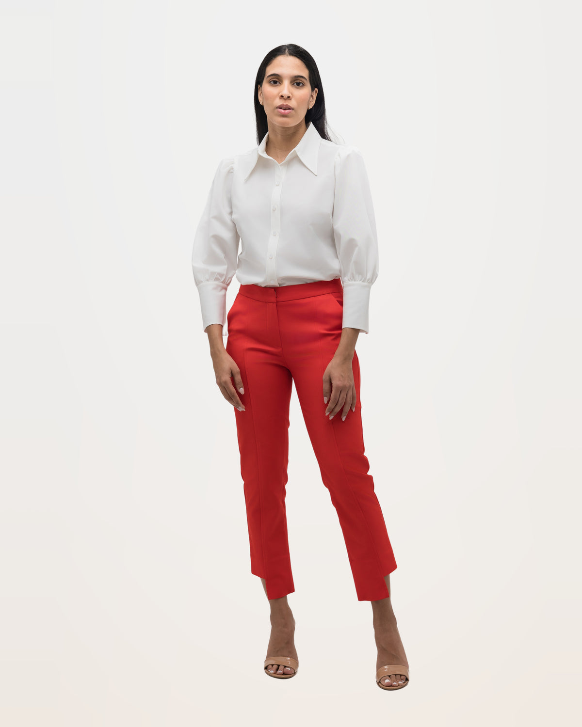 A woman in an off-white point-collar blouse tucked into red trousers, standing full length.